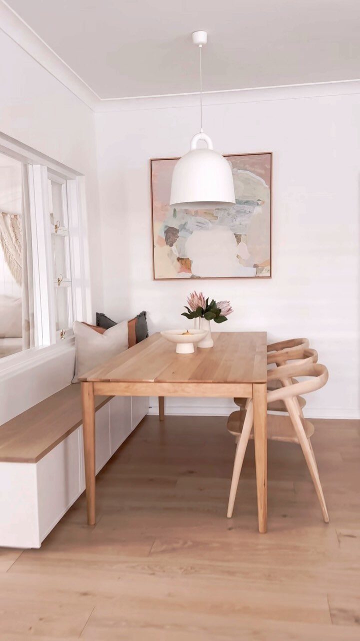 Built-in white cabinet bench with wooden seat next to a light wood dining table.