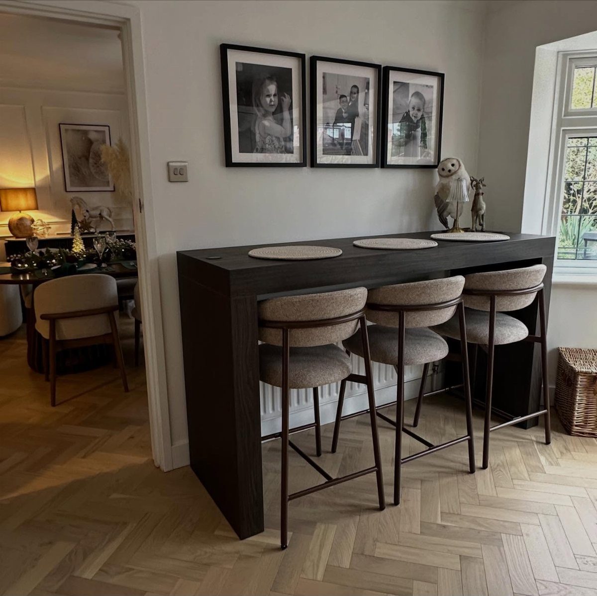 Dark wood breakfast bar with three grey stools against a white wall with portraits.