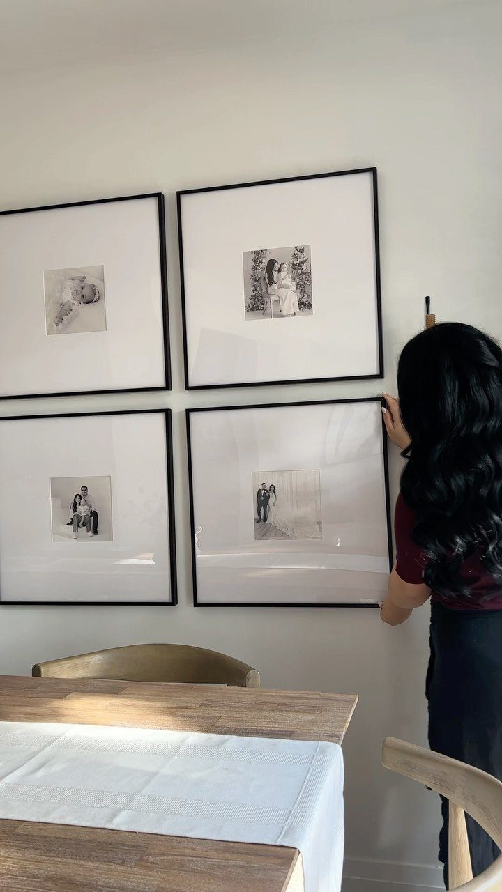 Four black-framed black and white photos arranged on a white wall above a table.