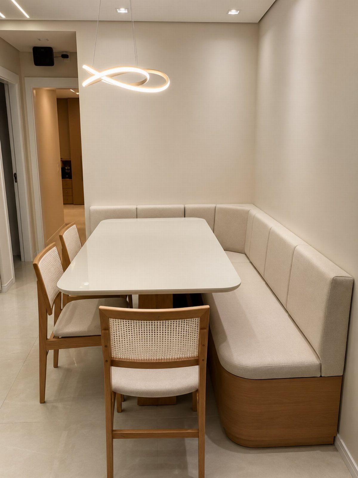 White dining table with a cream L-shaped banquette bench tucked into a wall niche.
