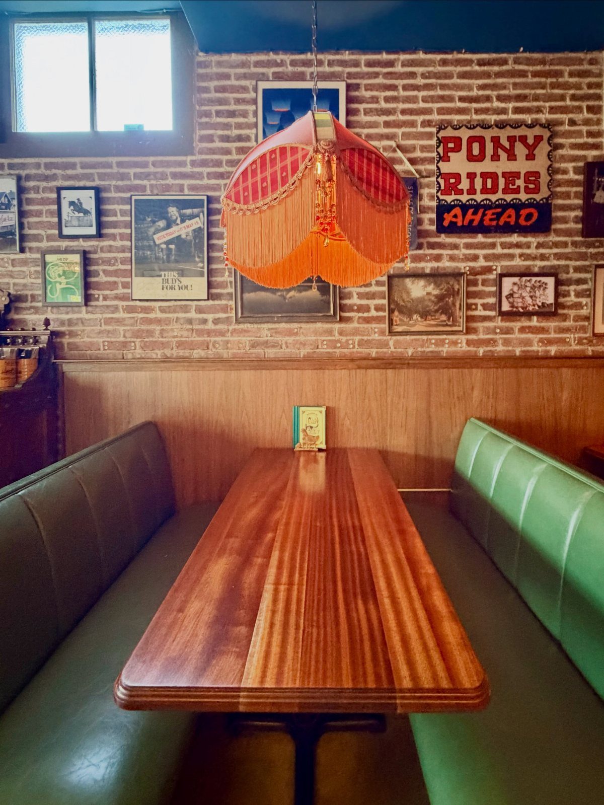 Green vinyl restaurant booth with a long wooden table and brick wall background.