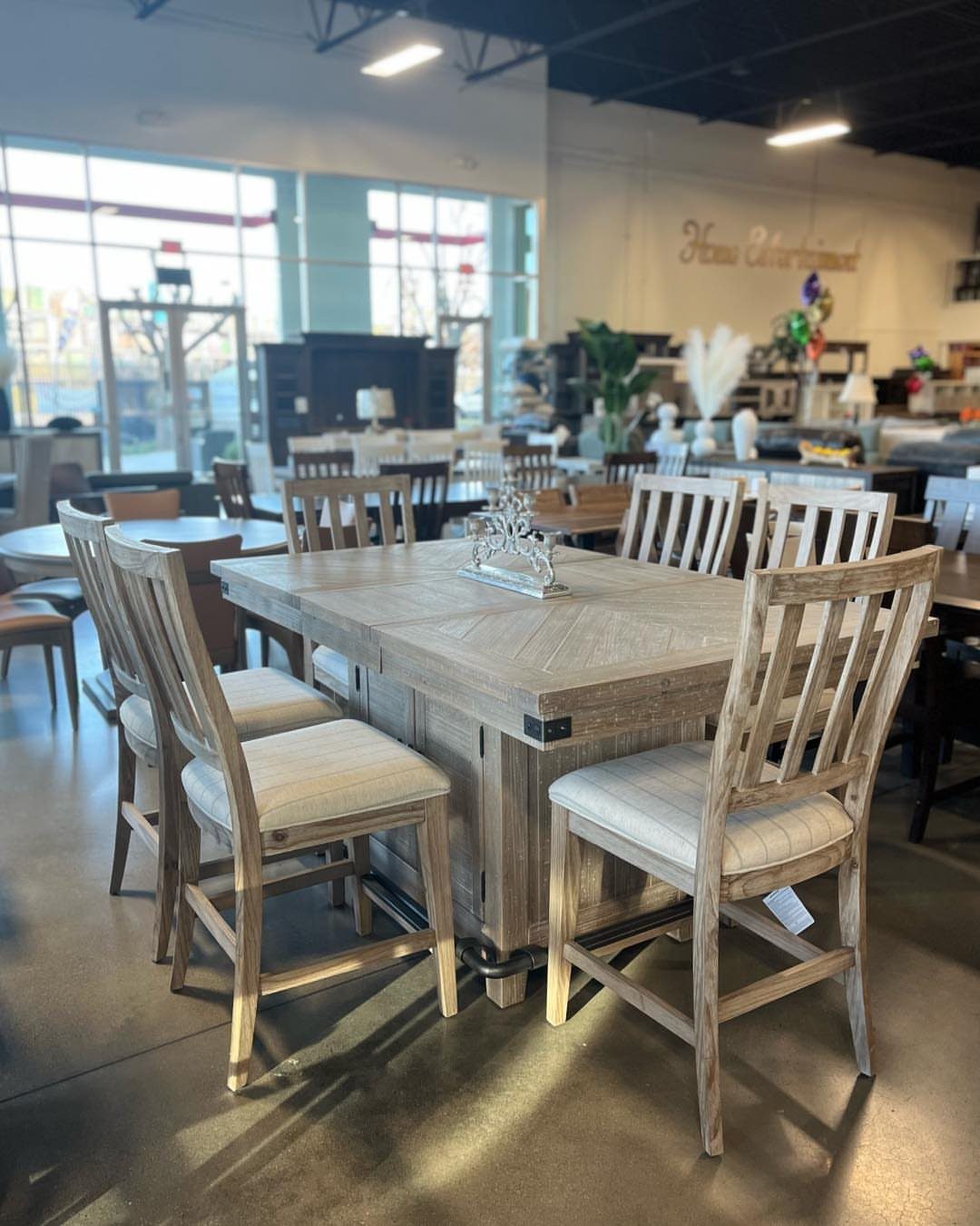 Counter height dining table set with weathered wood finish and cream upholstered chairs.