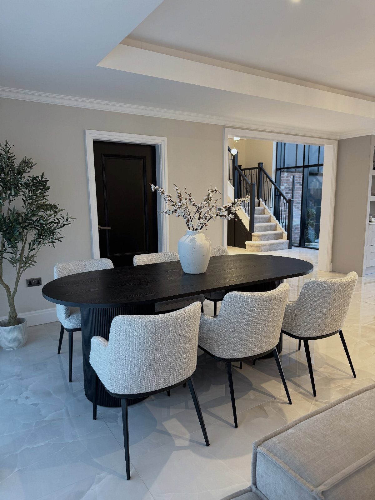 Oval black dining table with white textured chairs in a modern grey room.