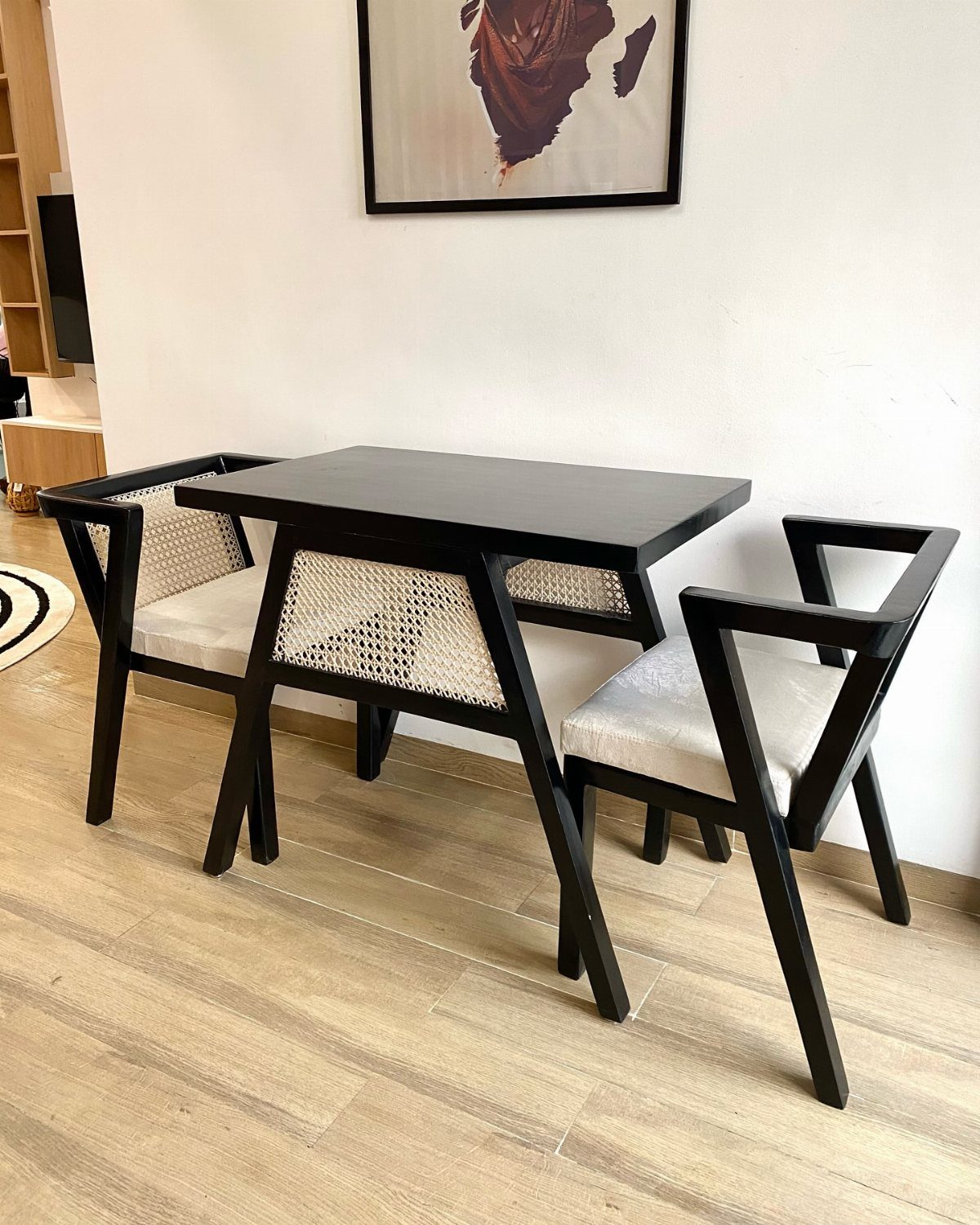 Black wooden dining table and two chairs with white cane backs on light flooring.