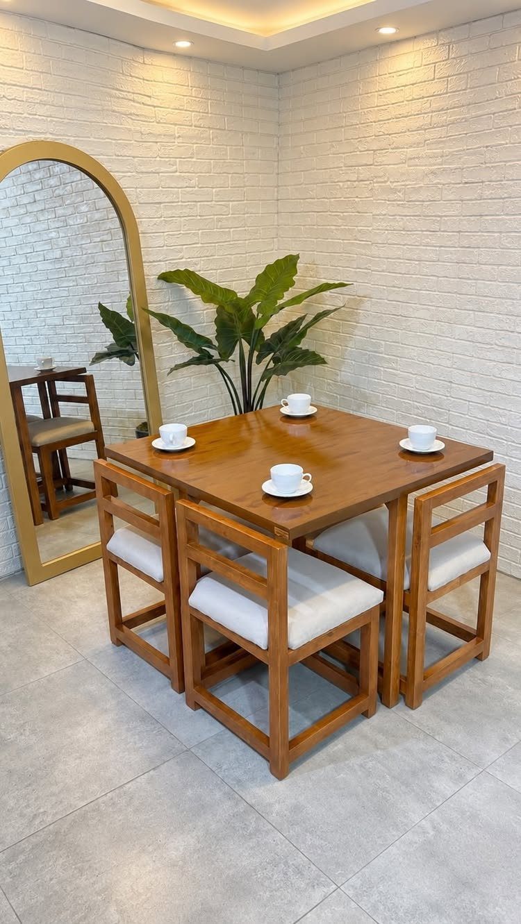 Wooden square dining table set with four white cushioned chairs in a bright room.