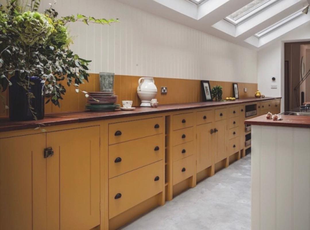 Dark reddish-brown wood countertops on yellow kitchen cabinets with white paneled walls.