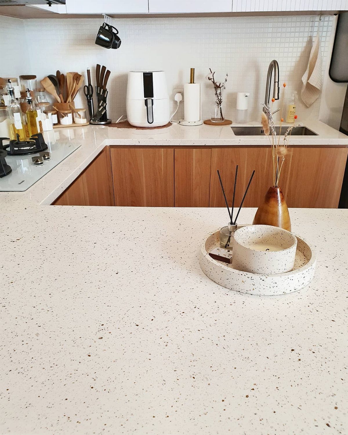 White speckled kitchen countertop with wooden cabinets, coffee maker, and decorative candle tray.