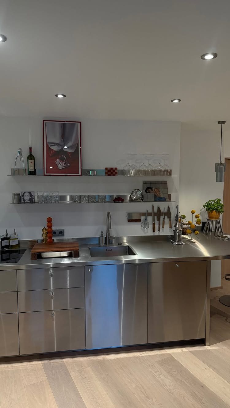 Stainless steel kitchen countertops and cabinets with a built-in sink and wall shelving.