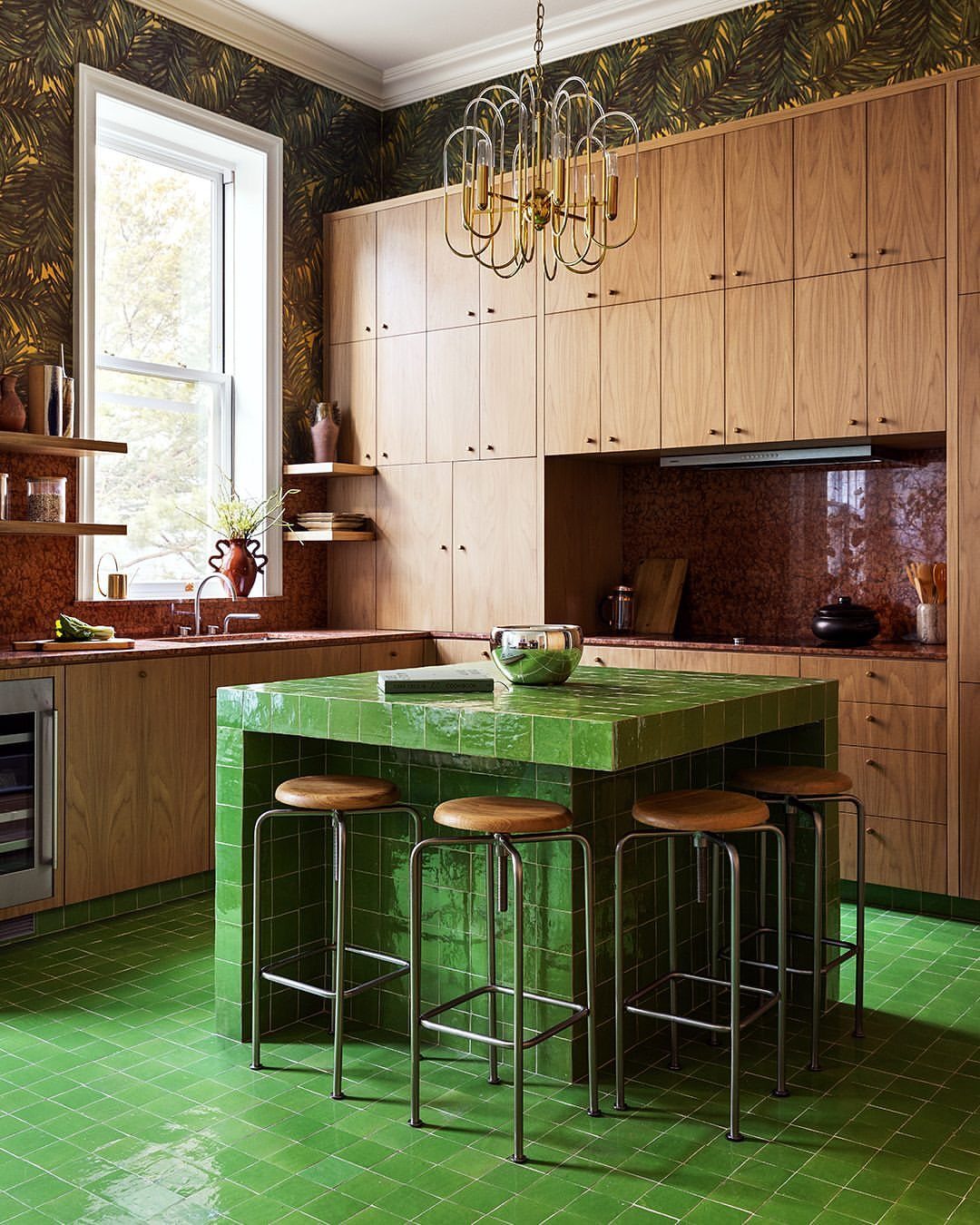 Green tiled kitchen island with wooden bar stools and light wood cabinetry.