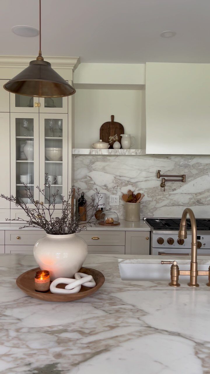 35 Farmhouse Kitchen Remodel Ideas Worth Stealing 12 White marble countertops and backsplash in a bright farmhouse kitchen with brass fixtures.