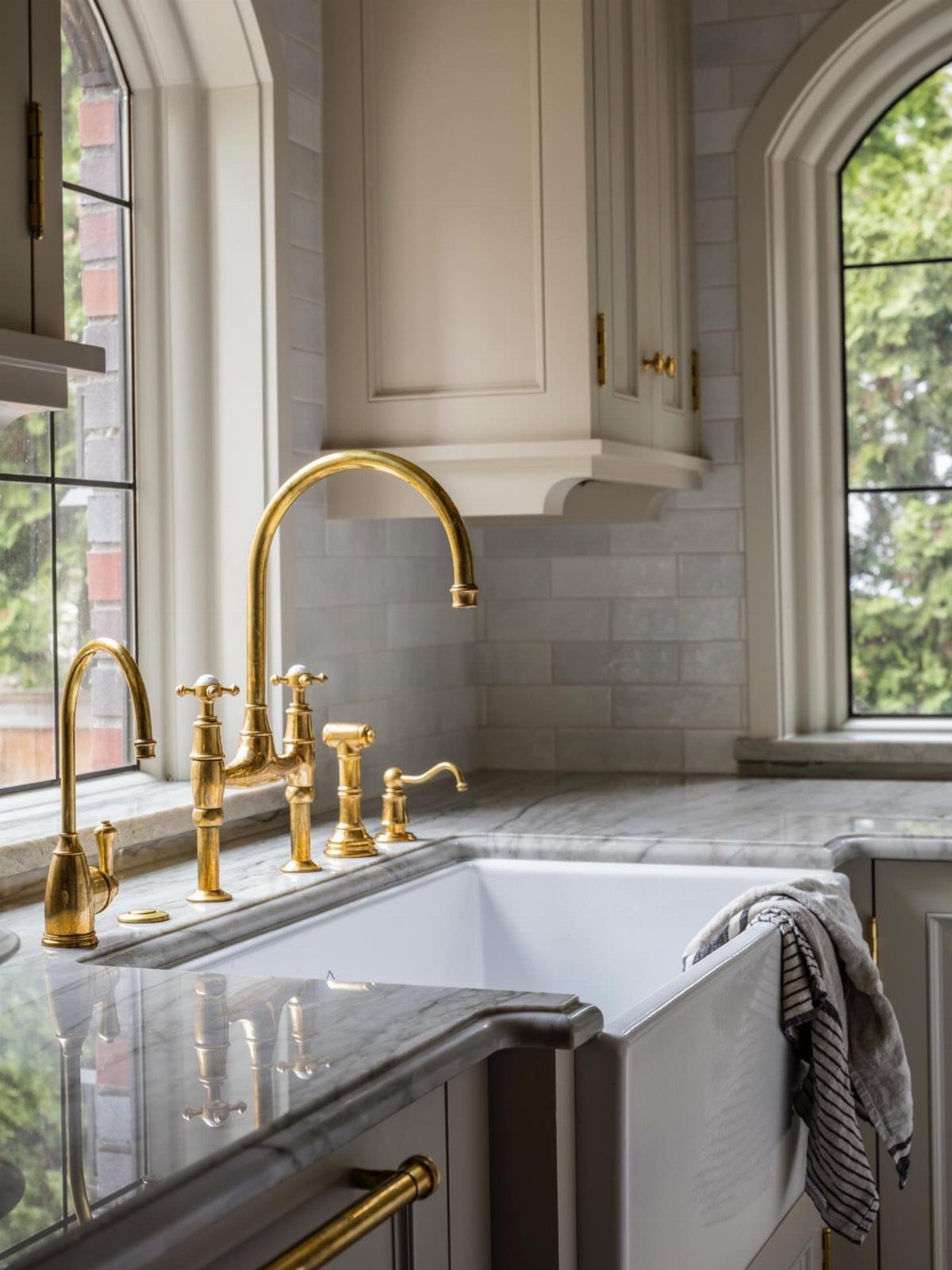 35 Farmhouse Kitchen Remodel Ideas Worth Stealing 16 Gold farmhouse faucet installed on a marble countertop over a white apron-front sink.