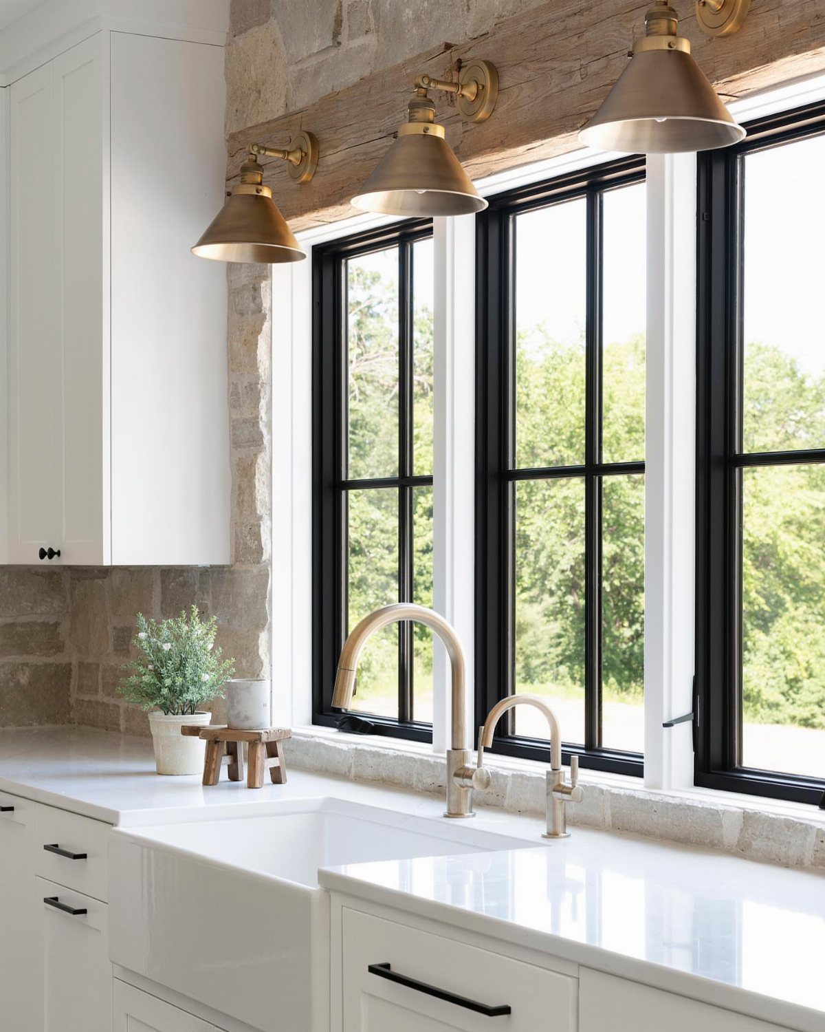 35 Farmhouse Kitchen Remodel Ideas Worth Stealing 18 Natural stone backsplash in a bright kitchen with white cabinets and brass lighting.
