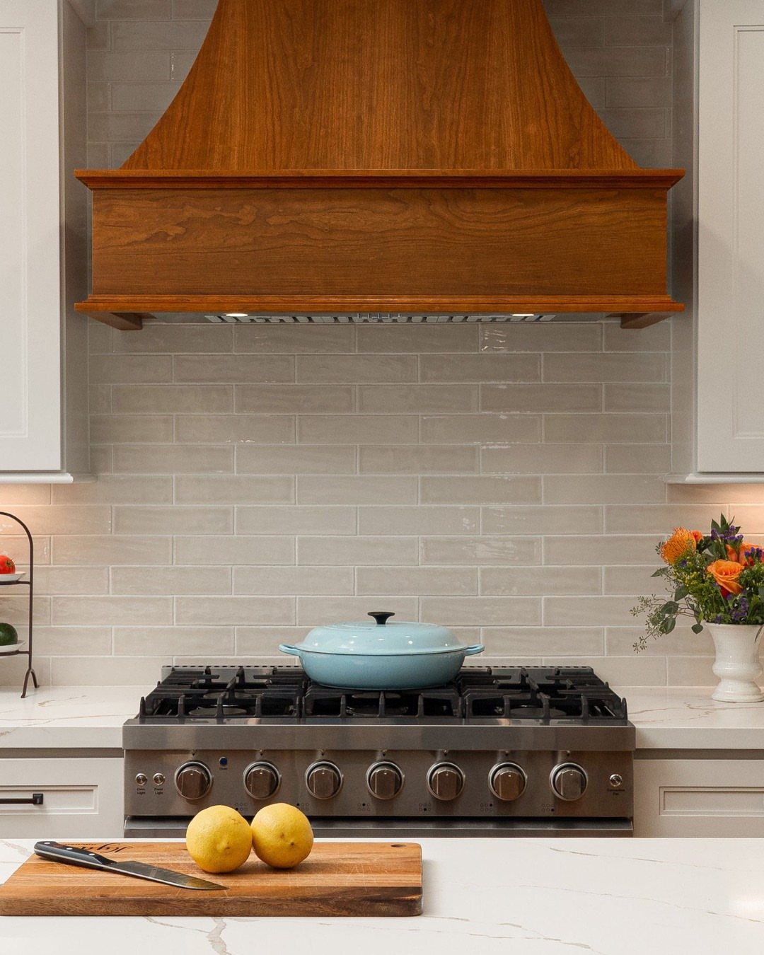 35 Farmhouse Kitchen Remodel Ideas Worth Stealing 8 White shaker cabinets and a wooden range hood above a stainless steel gas stove.