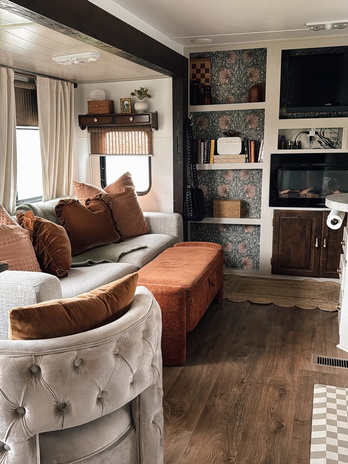 23 Fifth Wheel Remodel Ideas for Storage, Color, and Comfort 2 Remodeled RV interior with built-in vertical shelves, beige armchair, and orange storage ottoman.