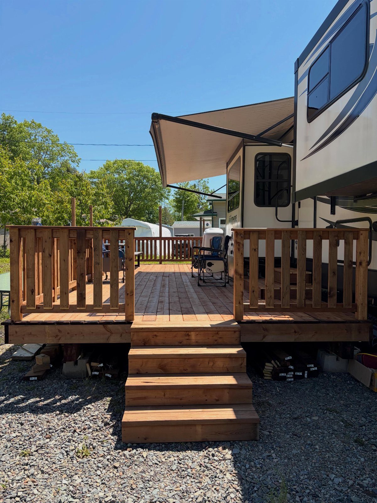 23 Fifth Wheel Remodel Ideas for Storage, Color, and Comfort 14 Wooden deck with stairs attached to a white fifth wheel RV under an awning.