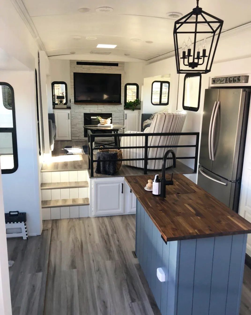 23 Fifth Wheel Remodel Ideas for Storage, Color, and Comfort 10 Remodeled fifth wheel interior with blue kitchen island and raised living room area.