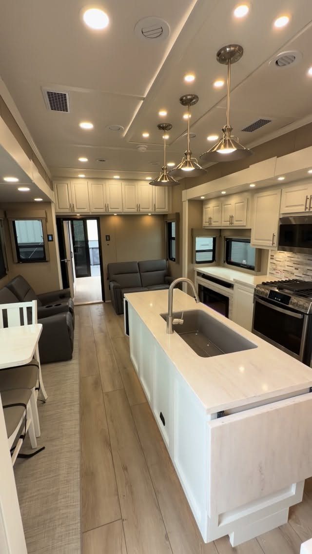 23 Fifth Wheel Remodel Ideas for Storage, Color, and Comfort 11 Modern RV interior with white kitchen island, cabinetry, and grey living room seating.