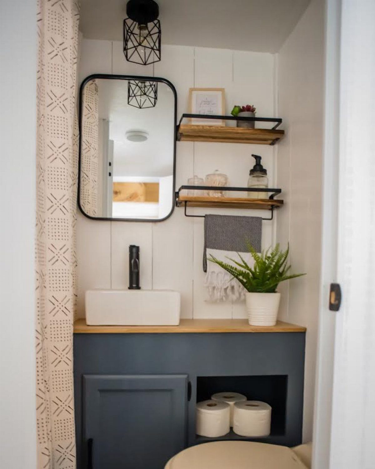 23 Fifth Wheel Remodel Ideas for Storage, Color, and Comfort 4 Small RV bathroom vanity with blue cabinets, white sink, and wooden wall shelves.