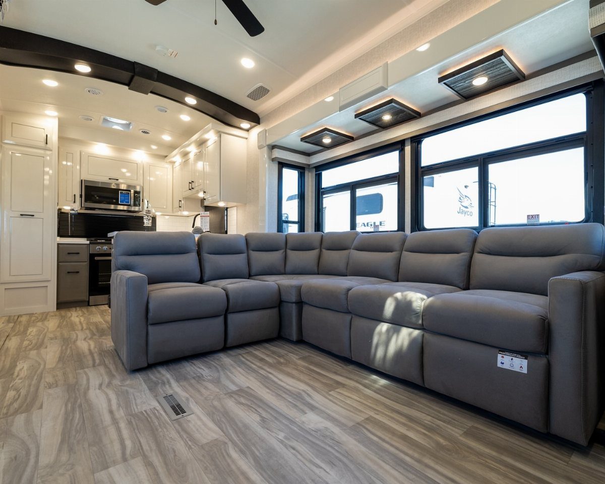 23 Fifth Wheel Remodel Ideas for Storage, Color, and Comfort 12 Grey sectional sofa and modern kitchen inside a spacious fifth wheel RV interior.