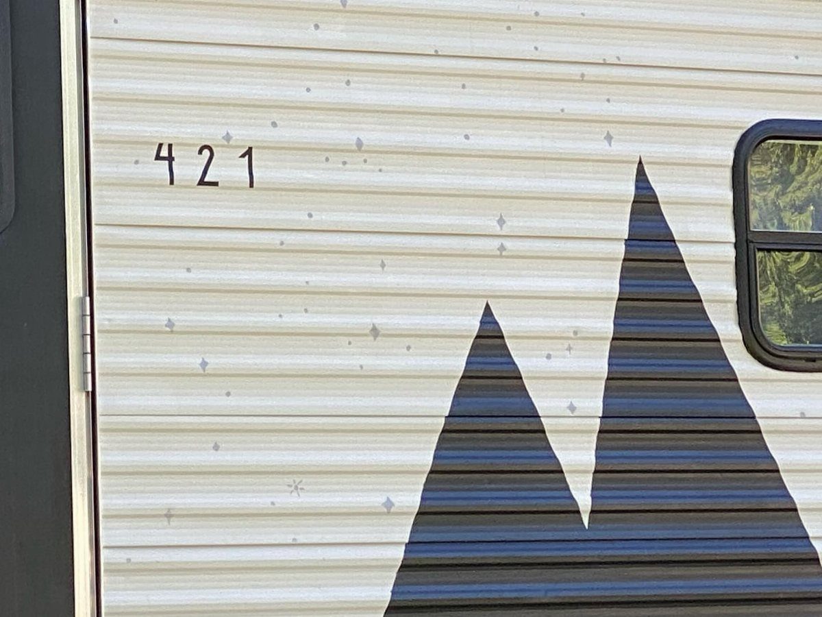 23 Fifth Wheel Remodel Ideas for Storage, Color, and Comfort 17 White RV exterior wall with a painted dark grey mountain silhouette and number 421.