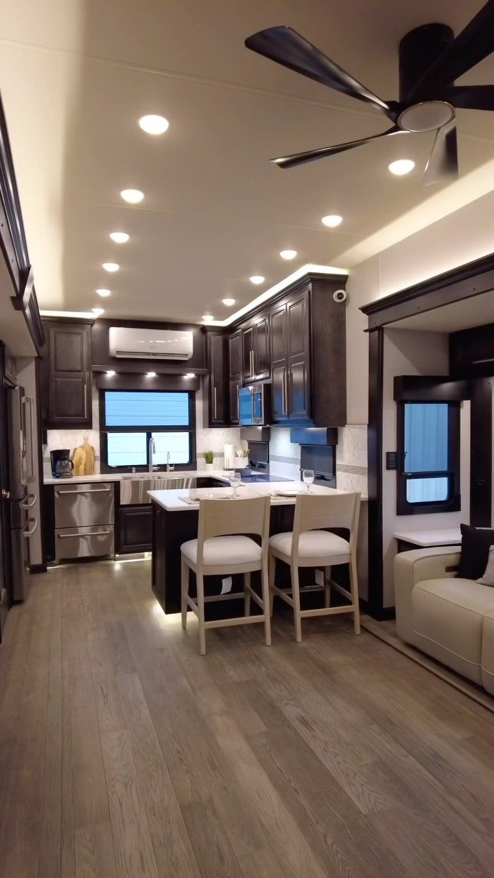 23 Fifth Wheel Remodel Ideas for Storage, Color, and Comfort 9 Modern RV kitchen with dark cabinets, light countertops, and a ceiling fan.