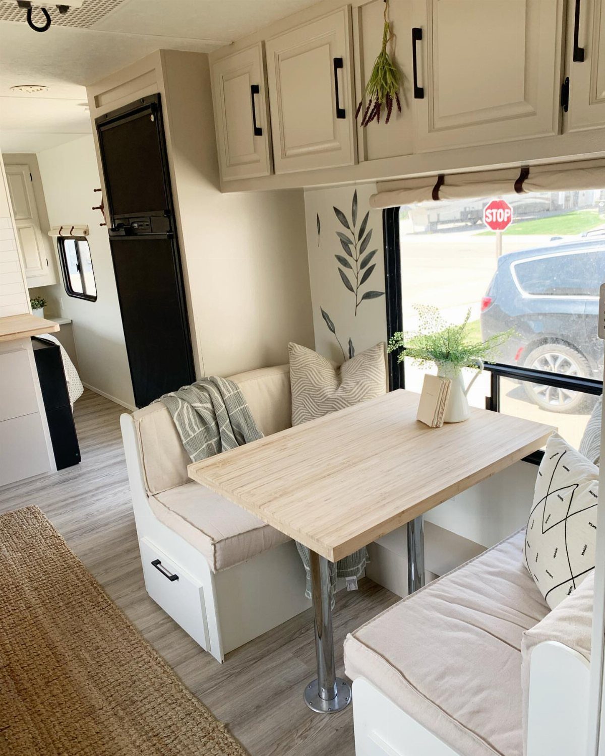 23 Fifth Wheel Remodel Ideas for Storage, Color, and Comfort 7 RV dinette with light wood table, beige seating, and white overhead cabinets.