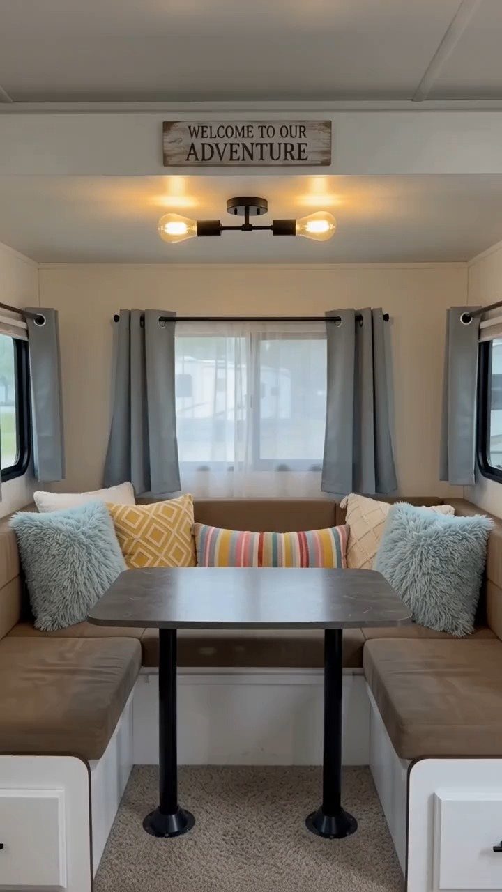 23 Fifth Wheel Remodel Ideas for Storage, Color, and Comfort 3 Modern three-bulb ceiling light fixture above a cozy RV dining nook with pillows.