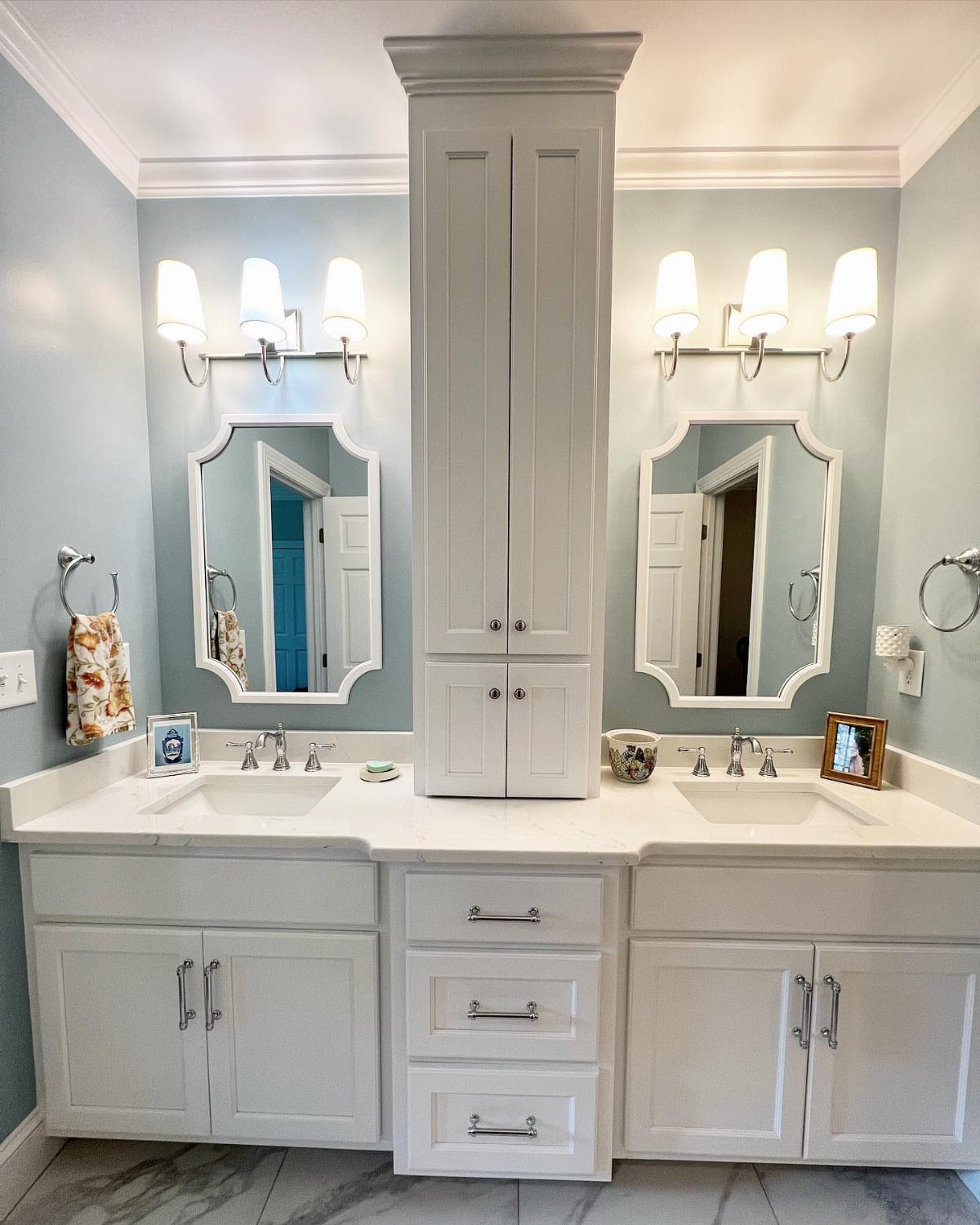 17 Jack and Jill Bathroom Remodel Ideas for Shared Spaces 1 White double vanity bathroom featuring a tall central built-in storage cabinet and light blue walls.