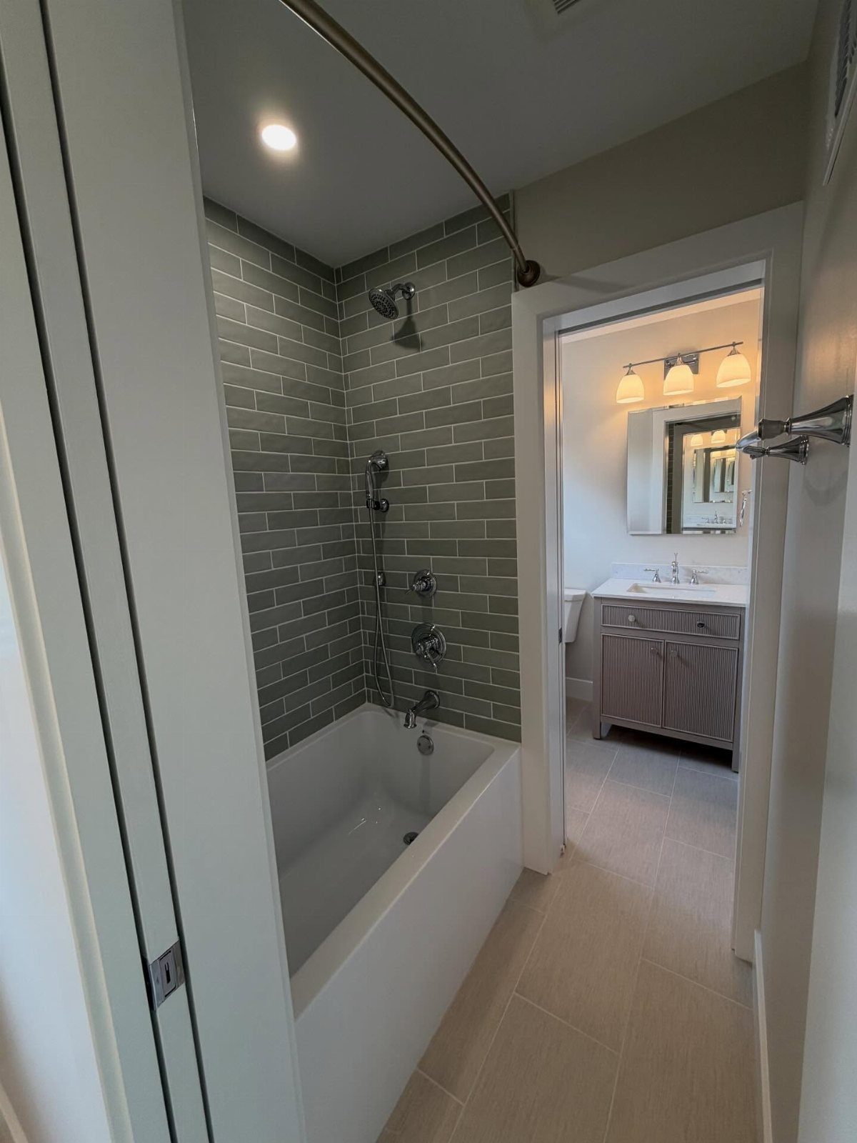 17 Jack and Jill Bathroom Remodel Ideas for Shared Spaces 8 White bathtub with grey subway tile walls and a view into a vanity area.