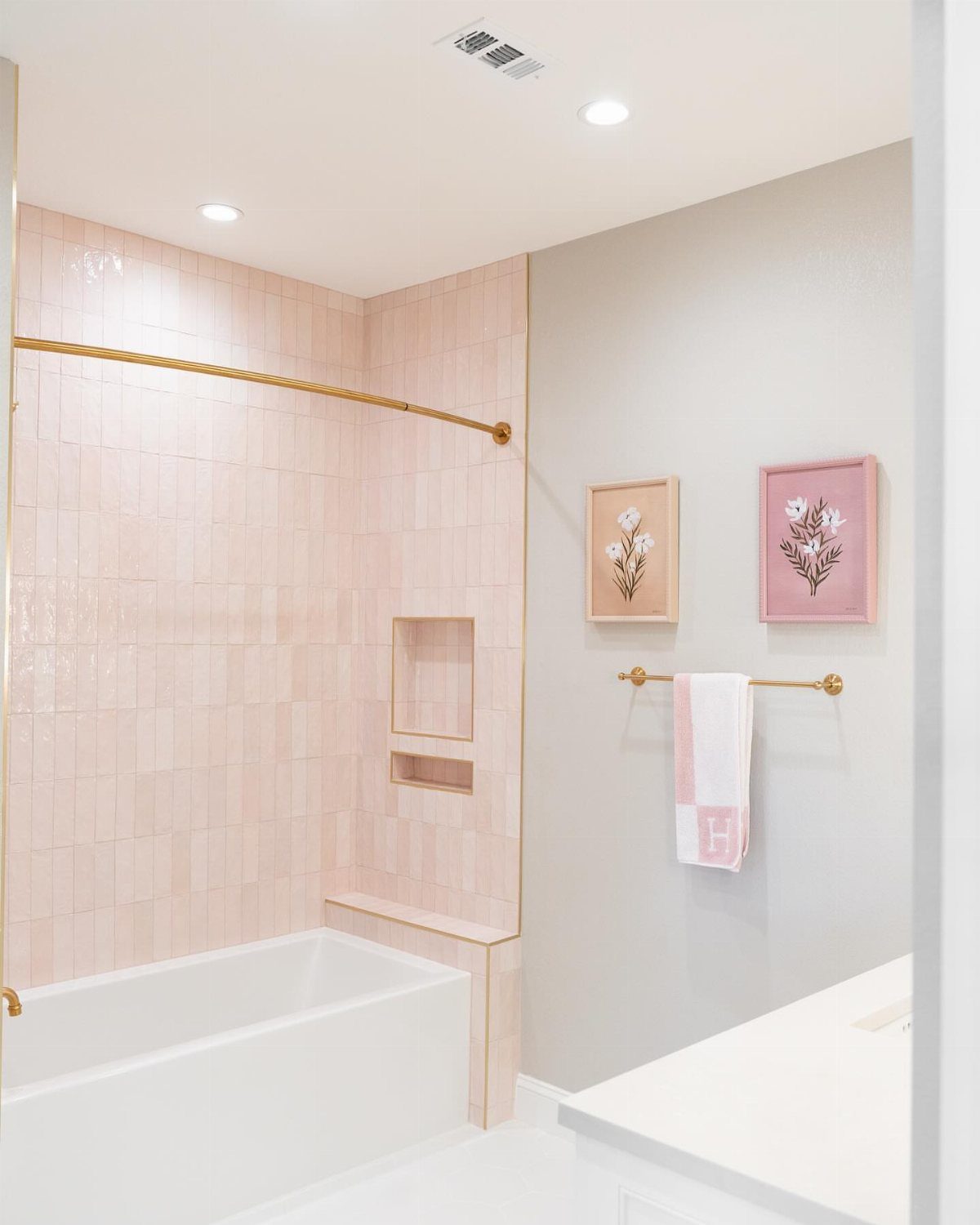 17 Jack and Jill Bathroom Remodel Ideas for Shared Spaces 16 White bathtub with pink tiled walls and floral art in a bright bathroom.
