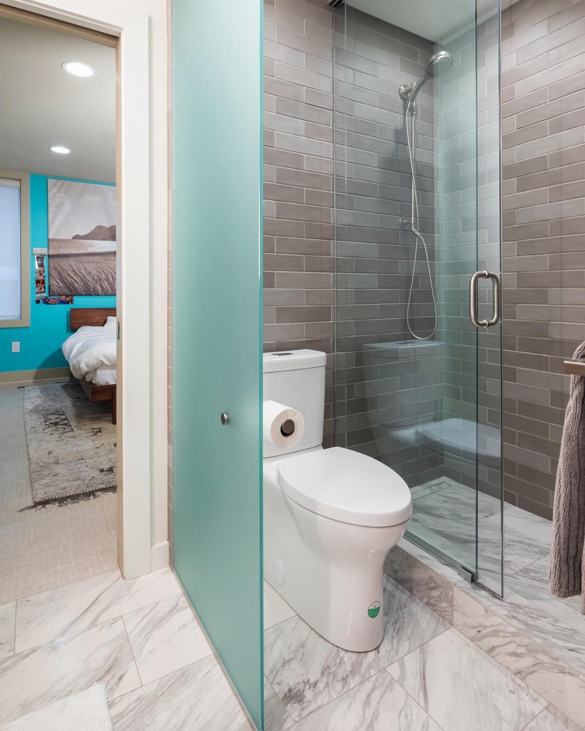 17 Jack and Jill Bathroom Remodel Ideas for Shared Spaces 9 Glass shower doors with silver hardware next to a white toilet and marble floors.