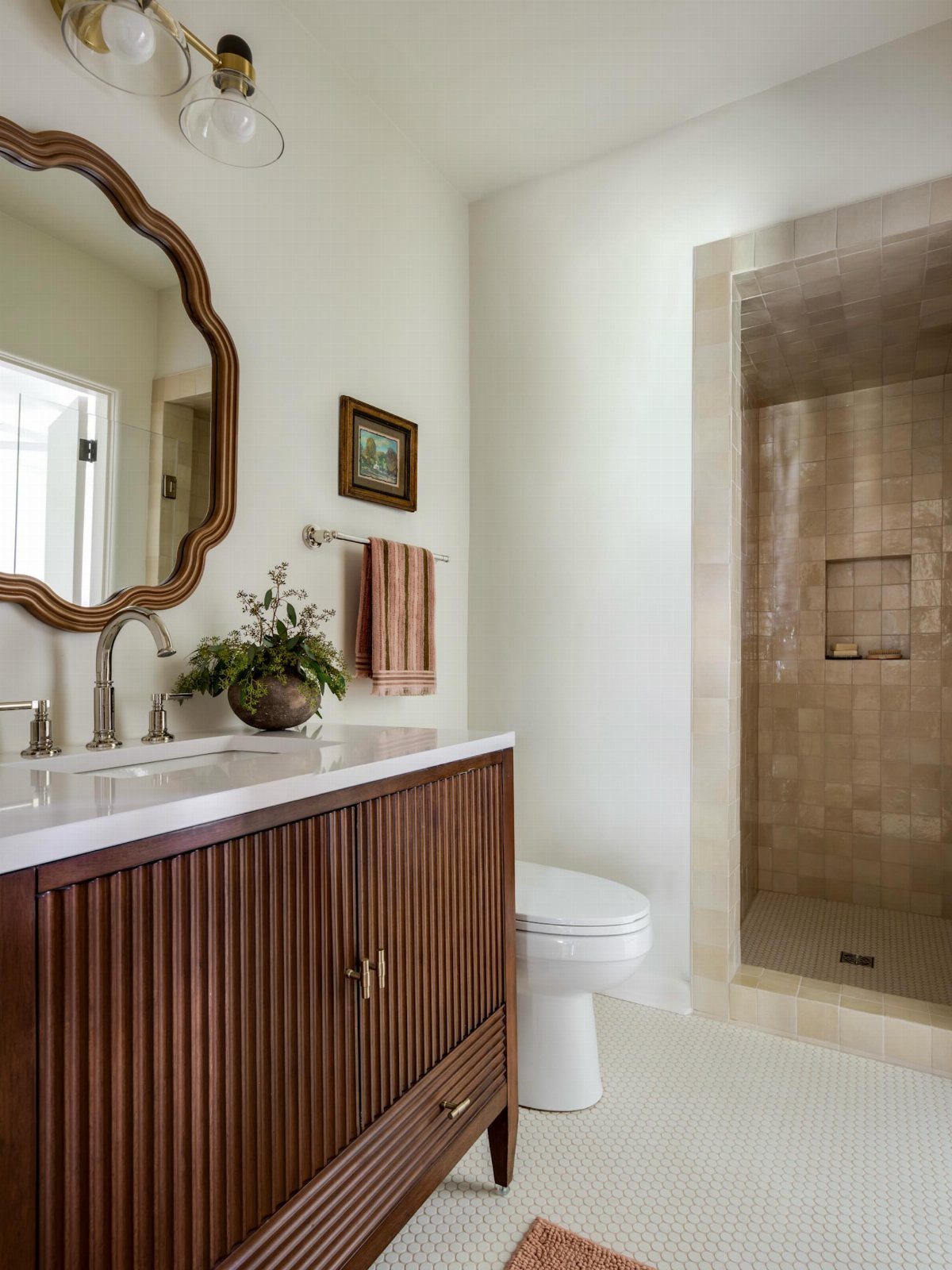 17 Jack and Jill Bathroom Remodel Ideas for Shared Spaces 17 Wooden bathroom vanity with white countertop, scalloped mirror, and walk-in tiled shower.