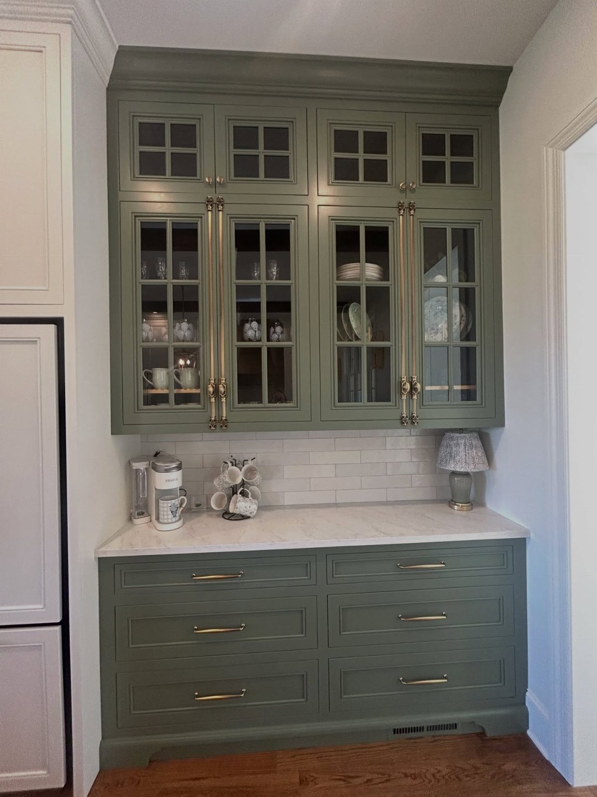 28 Kitchen Cabinets Remodel Ideas and Photos to Try in 2026 8 Sage green kitchen cabinets with glass-front upper doors and gold hardware handles.
