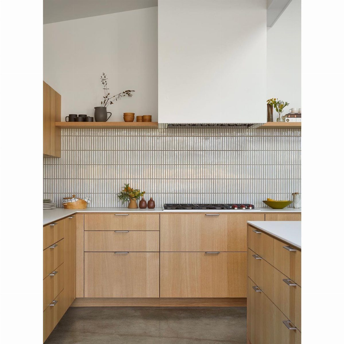 Light wood kitchen cabinets with white countertops and a vertical tiled backsplash.