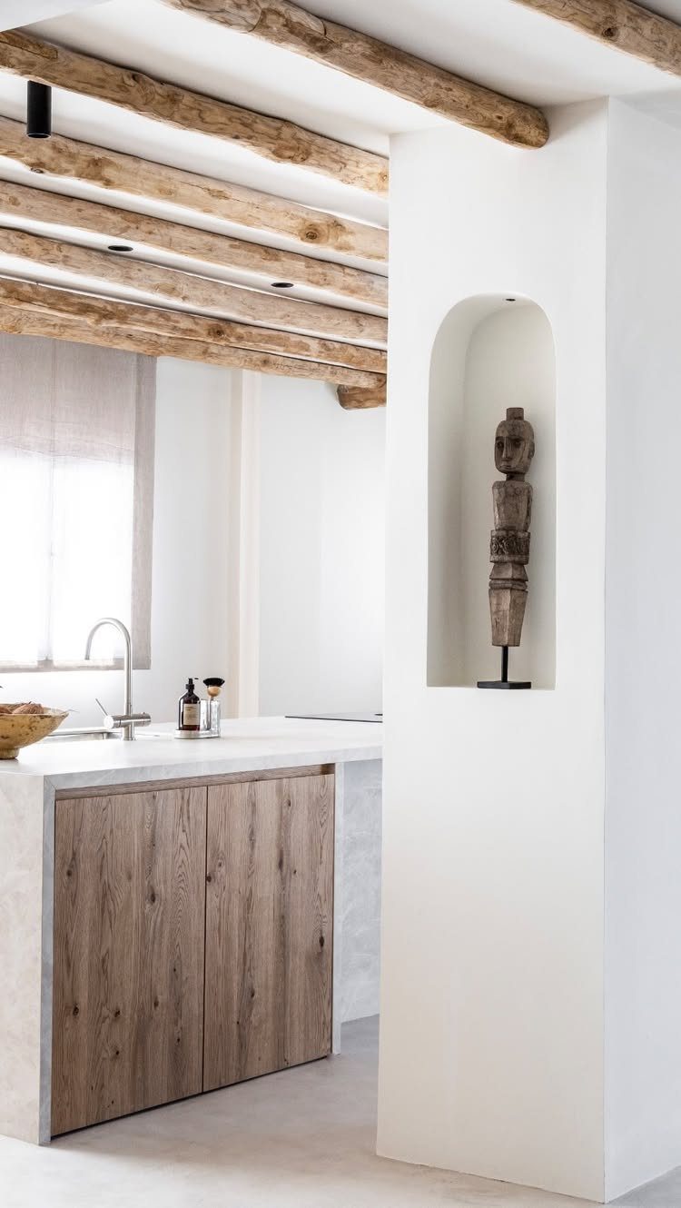 White kitchen with rustic wooden ceiling beams and a carved sculpture in an arch.