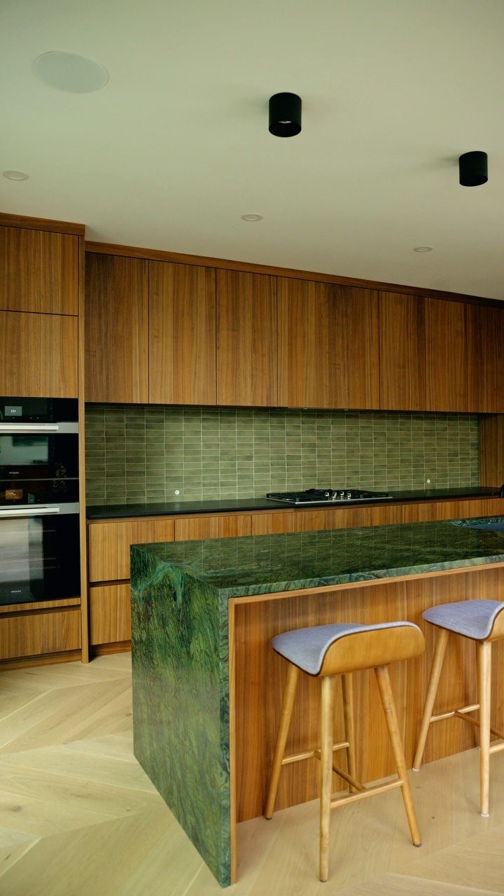 Kitchen with wood cabinets, green marble island, and light purple bar stools.