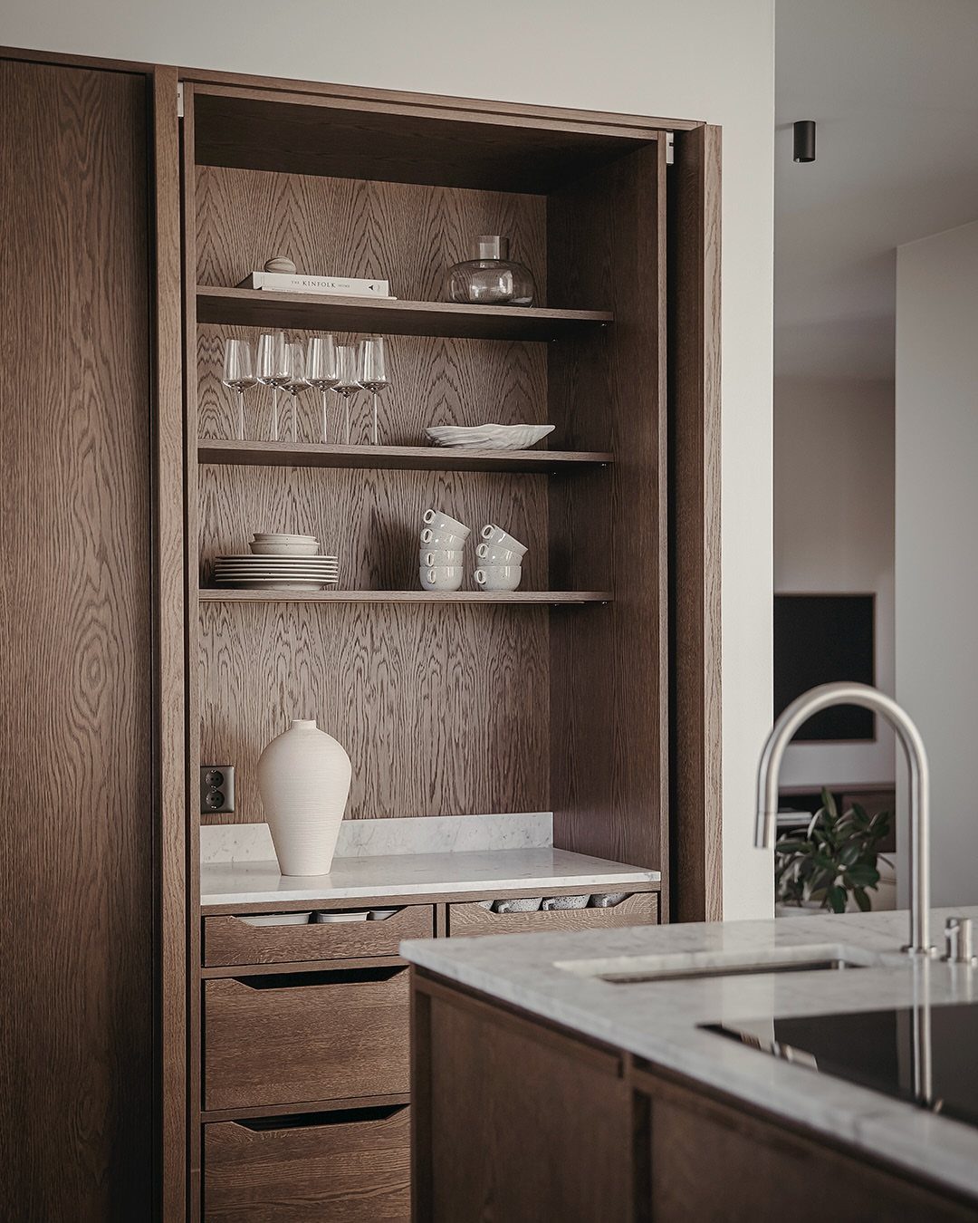 Medium-toned wood kitchen cabinets with open shelving holding white ceramics and glassware.