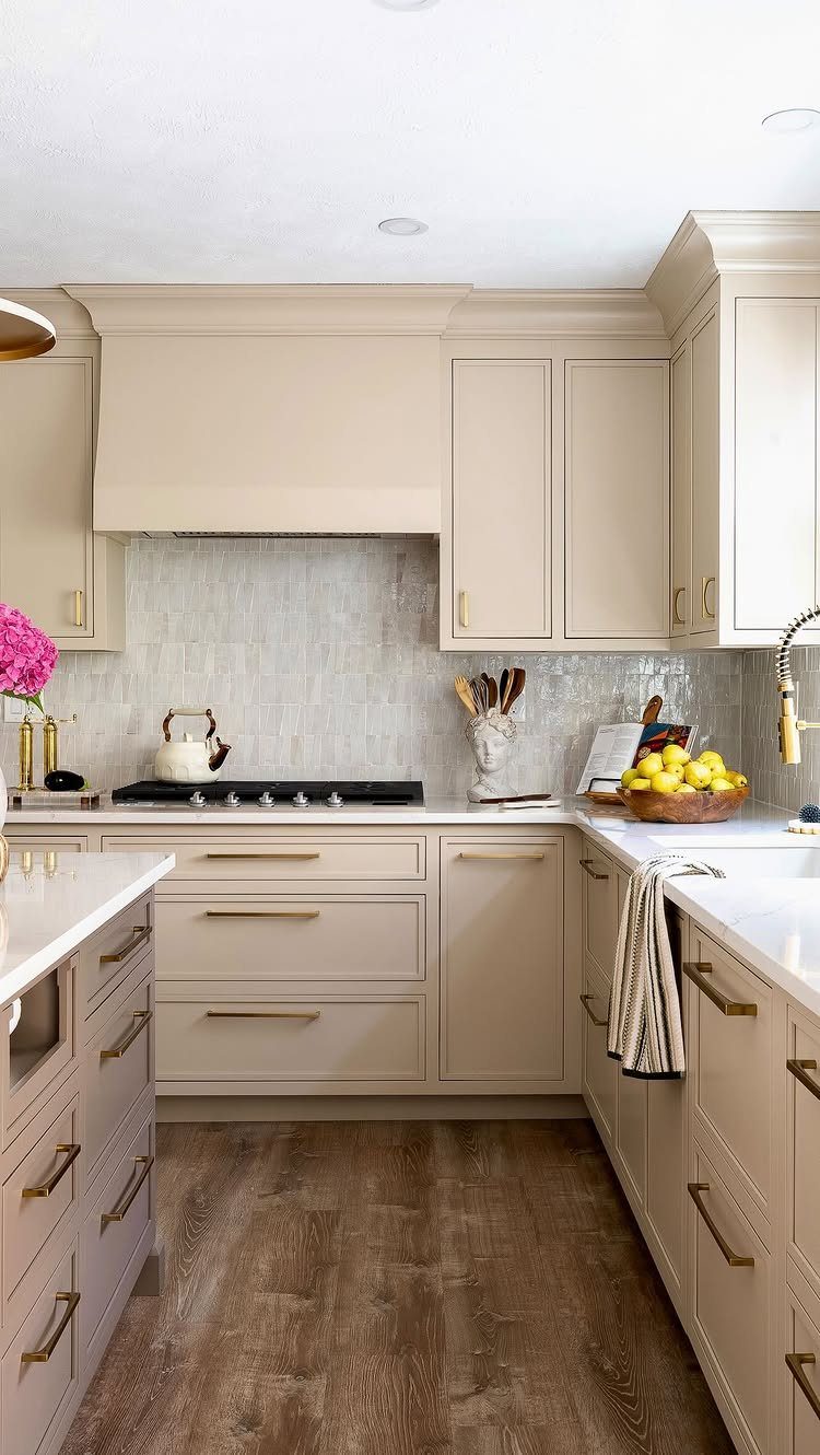 Soft neutral beige kitchen cabinets with gold handles and brown wood flooring.