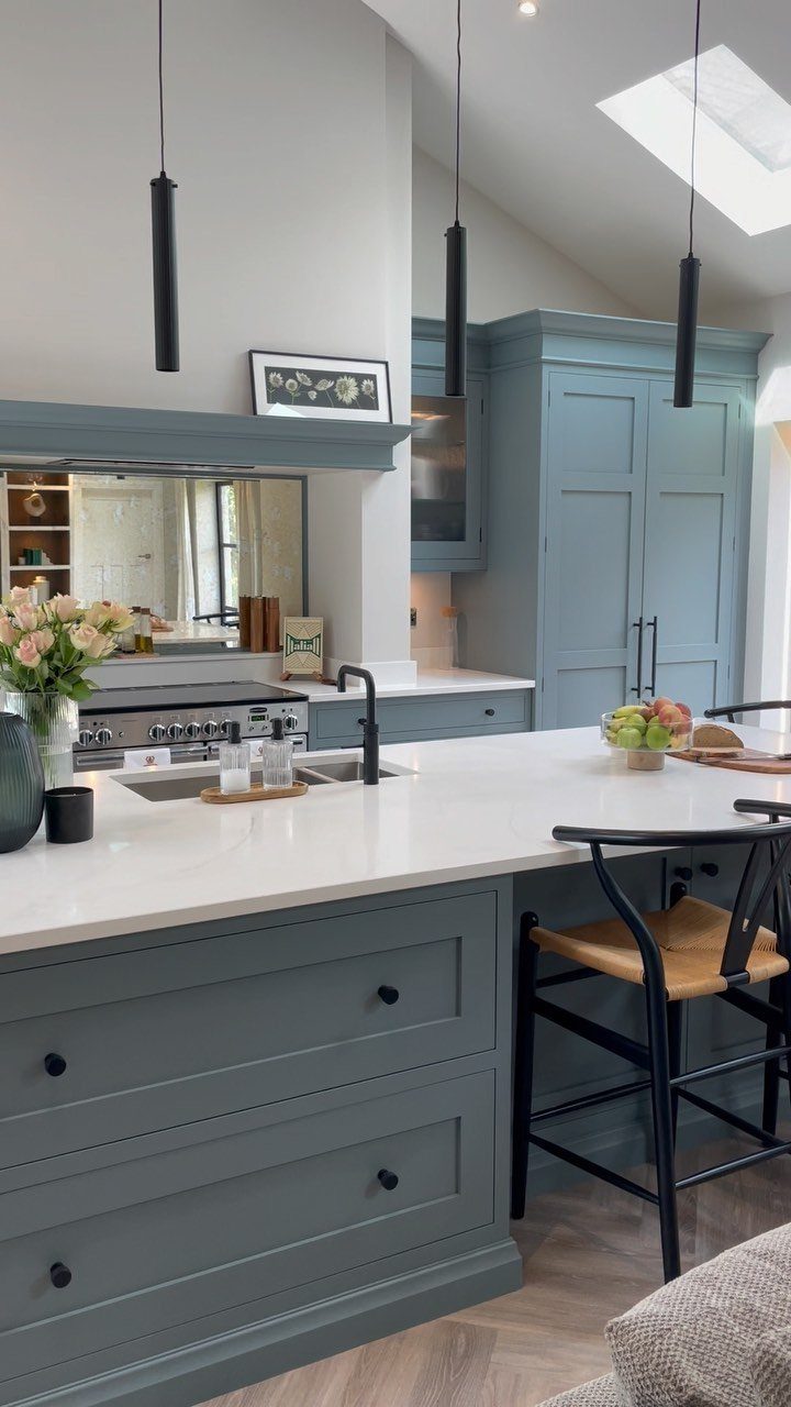 Muted blue-grey kitchen cabinets with white countertops and black modern pendant lighting.