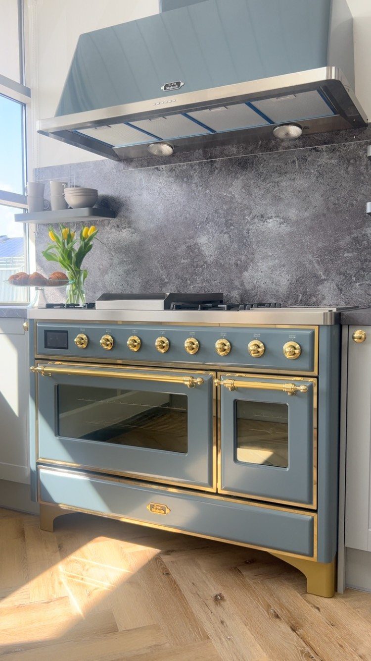 Blue kitchen range and vent hood against a grey stone backsplash and wood floor
