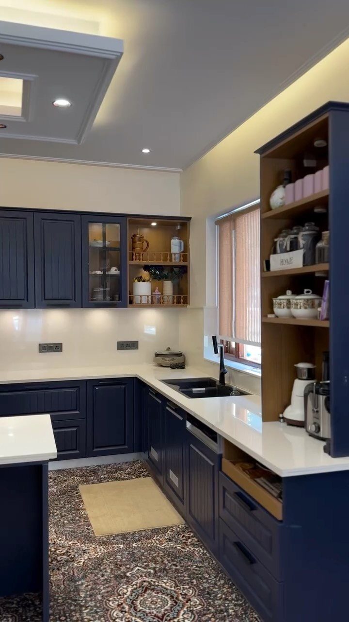 Navy blue kitchen cabinets with white countertops and a wooden open shelf unit.