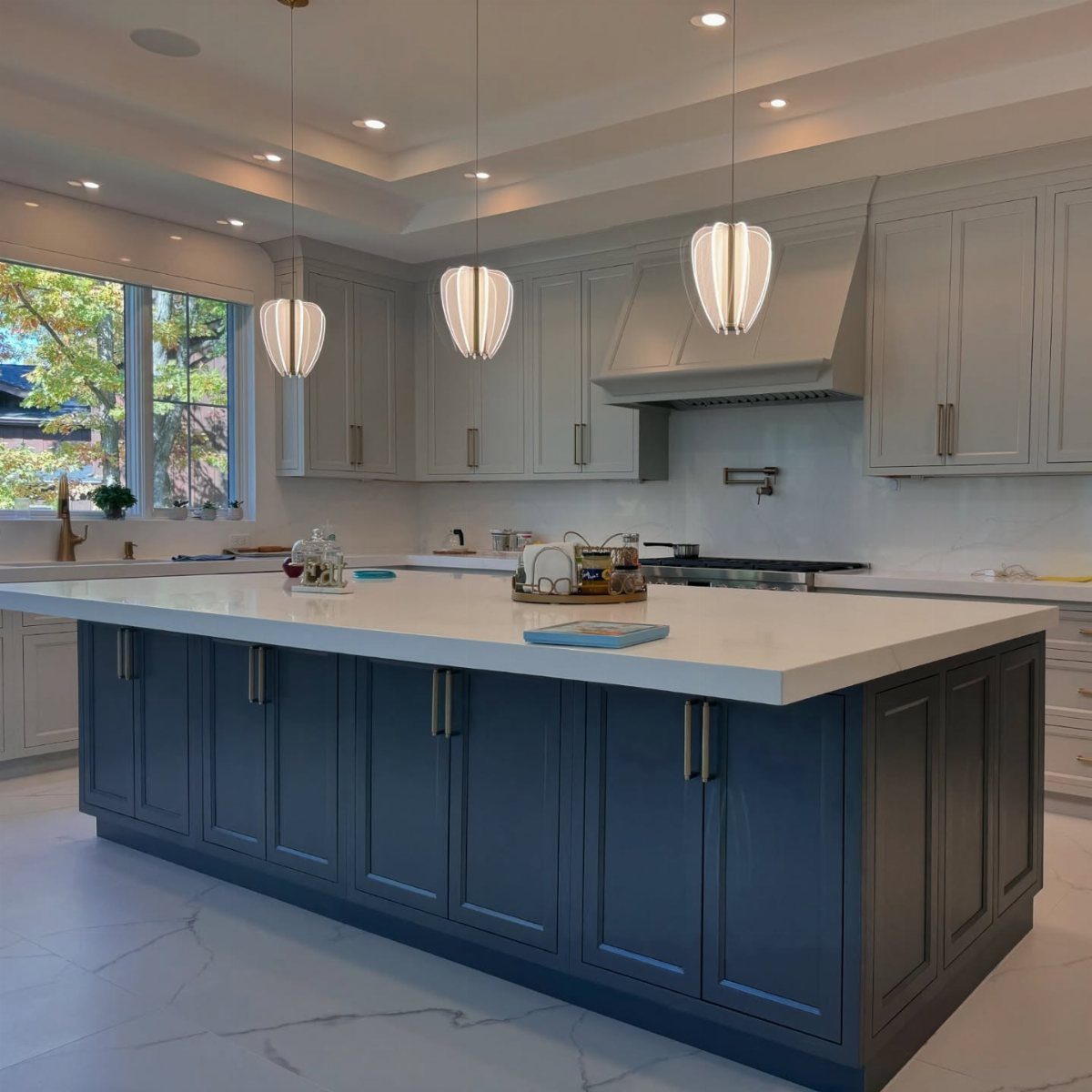Navy blue kitchen island with white countertop and light grey cabinetry and pendant lights.