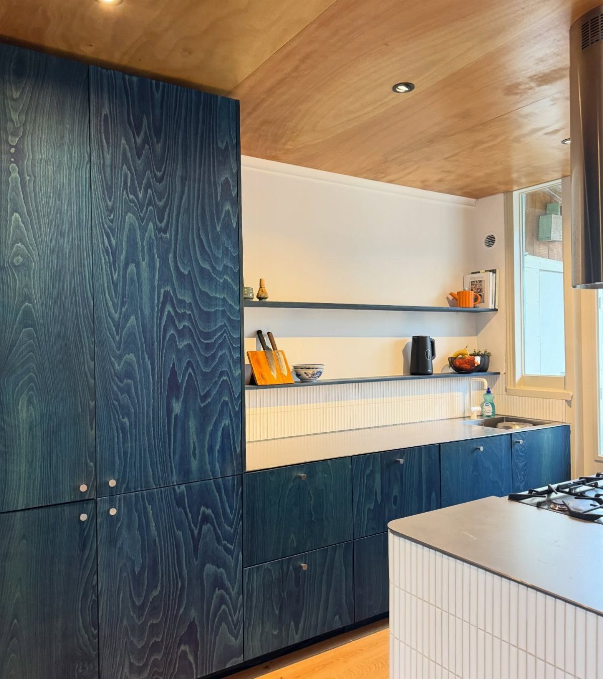 Deep blue wood-grain kitchen cabinets with white walls and a natural wood ceiling.