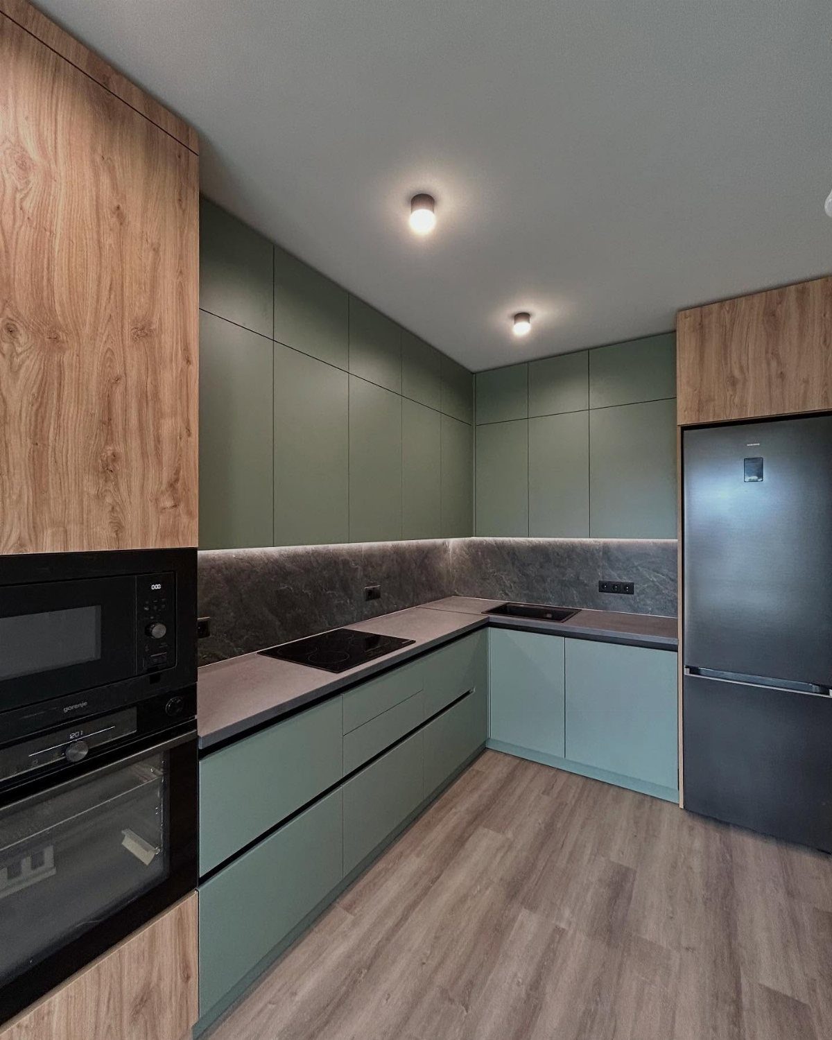 Sage green kitchen cabinets with grey countertops and light wood accents.