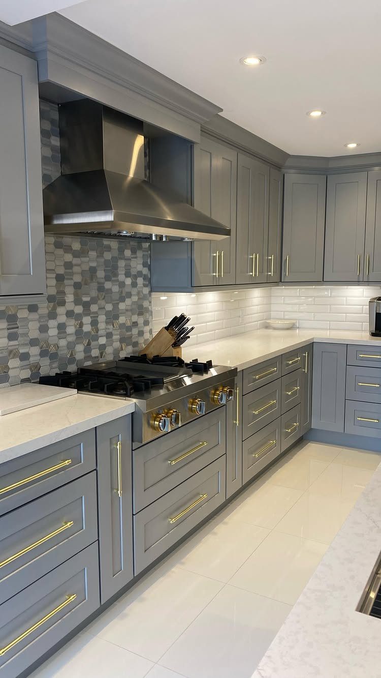 Grey kitchen cabinets with gold hardware and white countertops in a modern setting.