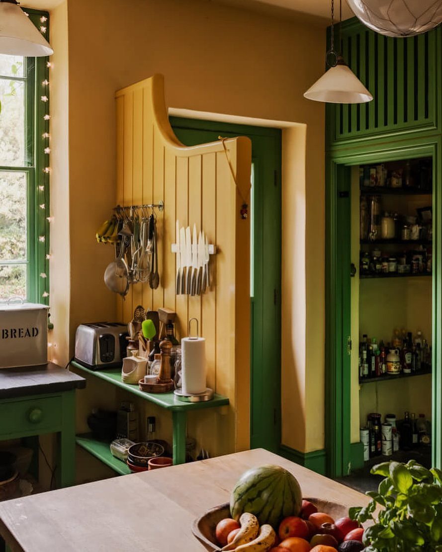 Yellow and green kitchen with wooden paneling, green cabinetry, and fresh fruit.