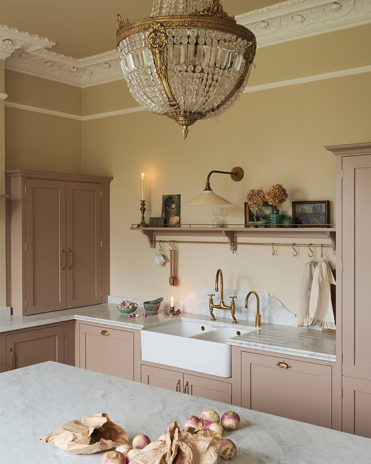 Dusty pink kitchen cabinets with white marble countertops and a crystal chandelier.