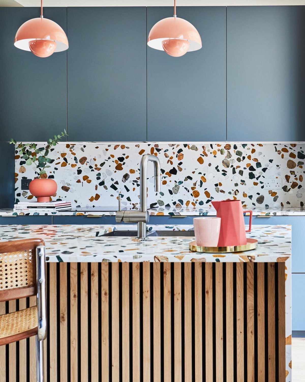 Blue-grey kitchen cabinets with a colorful terrazzo countertop and pink pendant lights.