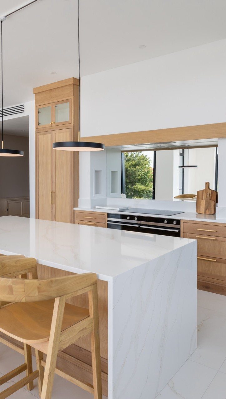 White marble kitchen island and countertops paired with light natural wood cabinetry and stools.