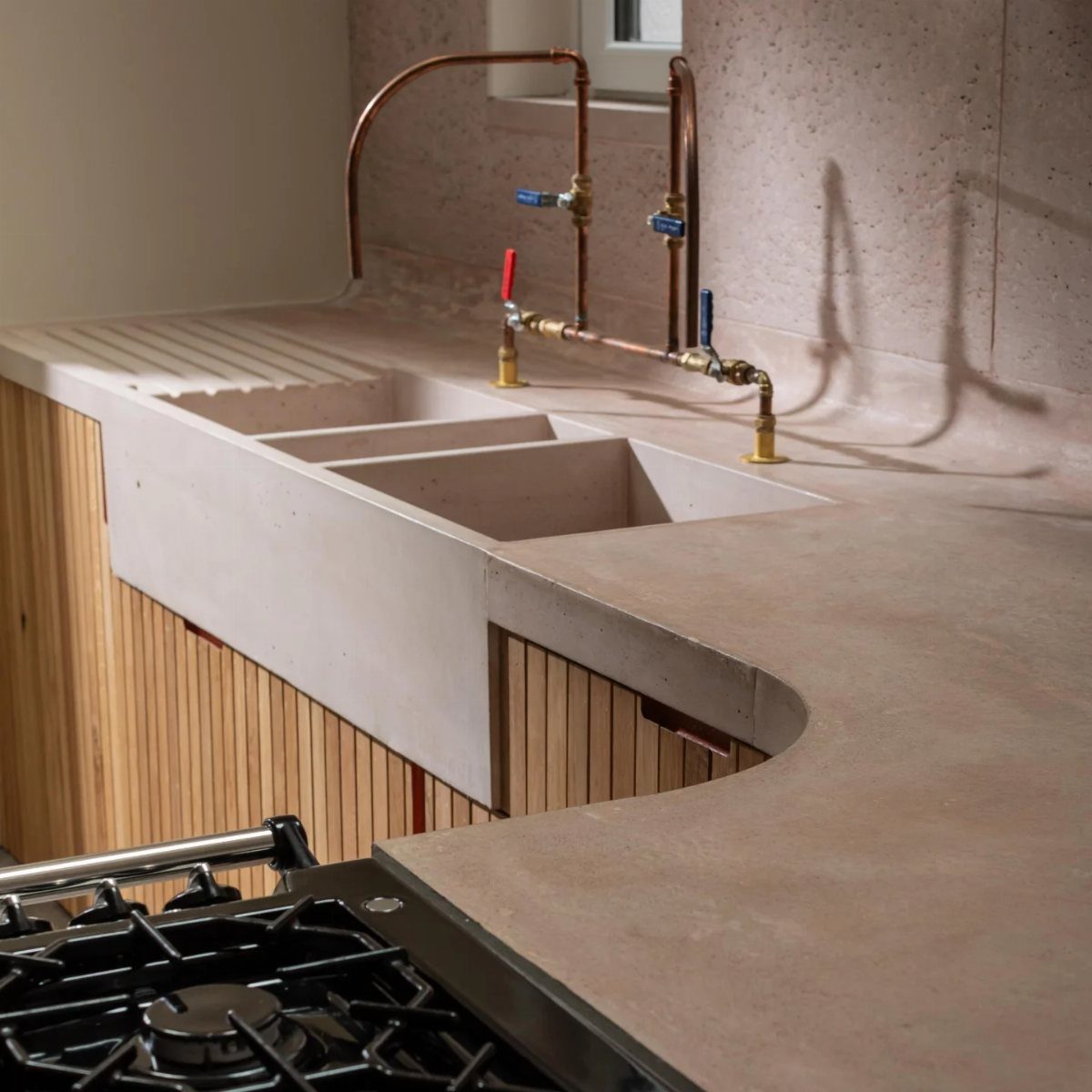 Light grey concrete countertops with an integrated double sink and copper piping faucet.